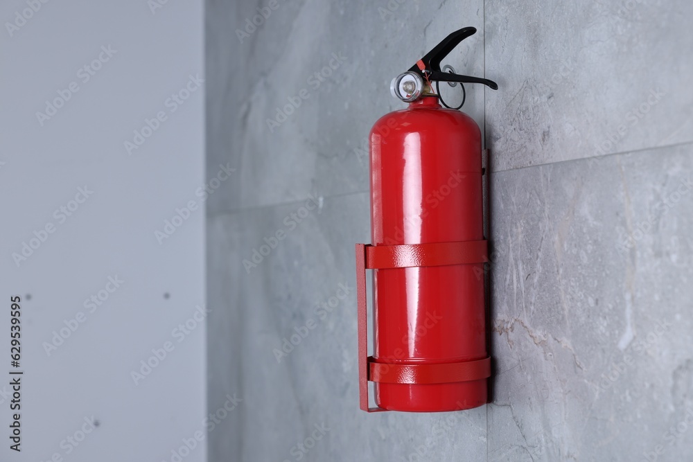 Obraz premium Fire extinguisher on grey wall, space for text