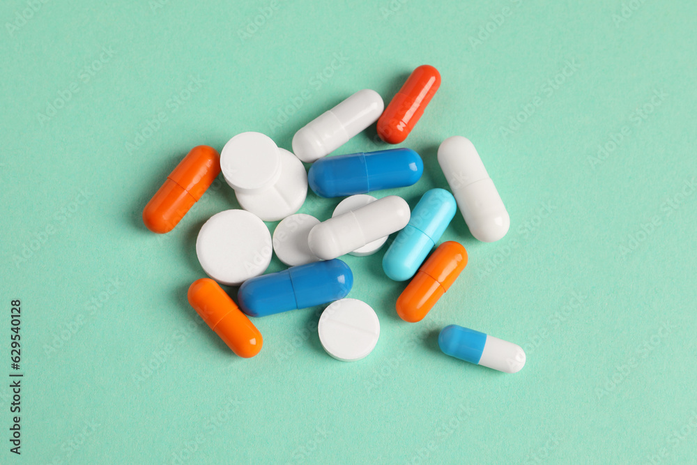 Pile of colorful pills on green background, flat lay