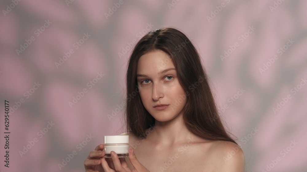 Attractive young girl with long hair holding a small jar of cream Attractive young girl with long hair holding a small jar of cream