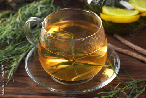 Cup of homemade herbal tea and fresh tarragon leaves on wooden table, closeup