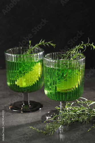 Glasses of homemade refreshing tarragon drink and sprigs on grey table photo