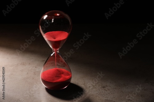 Hourglass with red flowing sand on grey table. Space for text