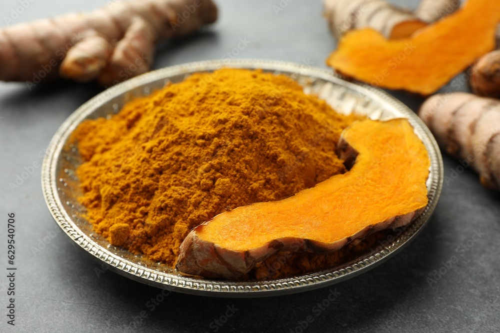 Plate with turmeric powder and cut root on grey table, closeup Plate with turmeric powder and cut root on grey table, closeup