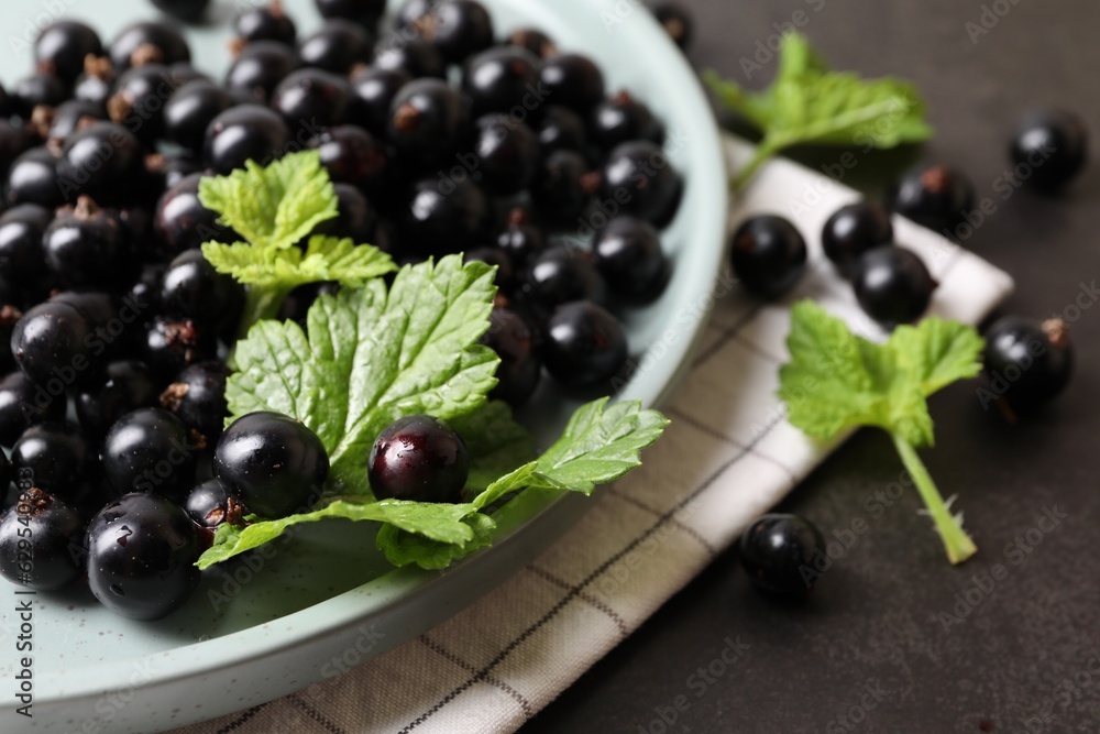 Plate with ripe blackcurrants and leaves on grey background, closeup Plate with ripe blackcurrants and leaves on grey background, closeup
