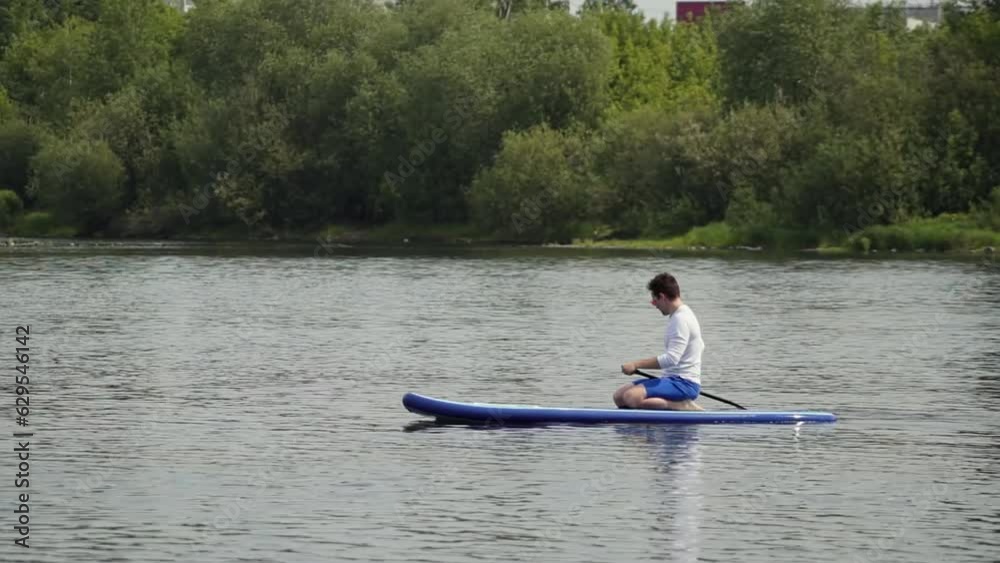 caucasian man on supboard. a man sits and rows with an oar on a board. a man in casual clothes floats on the river. High quality Full HD video recording caucasian man on supboard. a man sits and rows with an oar on a board. a man in casual clothes floats on the river. High quality Full HD video recording