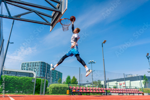 Tall guy basketball player jumps to the hoop with the ball in his hand to score a spectacular dunk during practice on the basketball court in the park © Guys Who Shoot