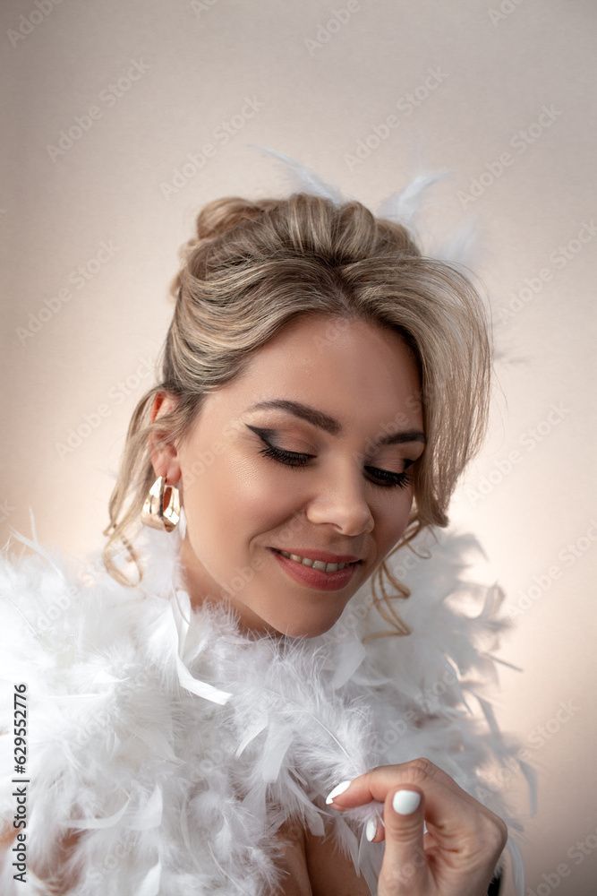 Portrait of a beautiful bride with a wedding hairstyle dressed in a white dress with feathers. A girl with a professional makeup against the wall