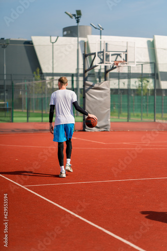 a Tall guy basketball player with the ball shows his dribbling skills during practice on the basketball court in the park  © Guys Who Shoot