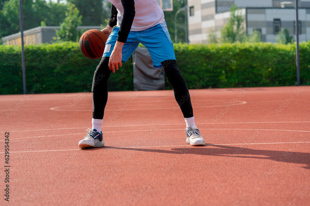 Fototapeta premium a Tall guy basketball player with the ball shows his dribbling skills during practice on the basketball court in the park 