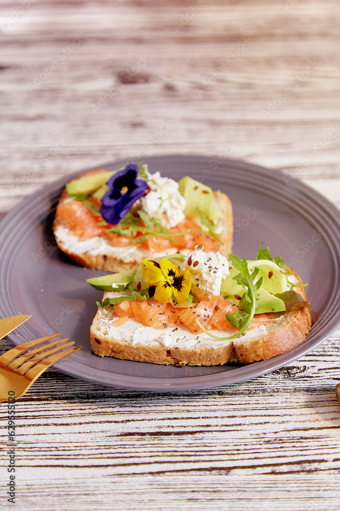 Healthy breakfast - toasts with salmon, avocado and edible flowers. Pescetarian diet.