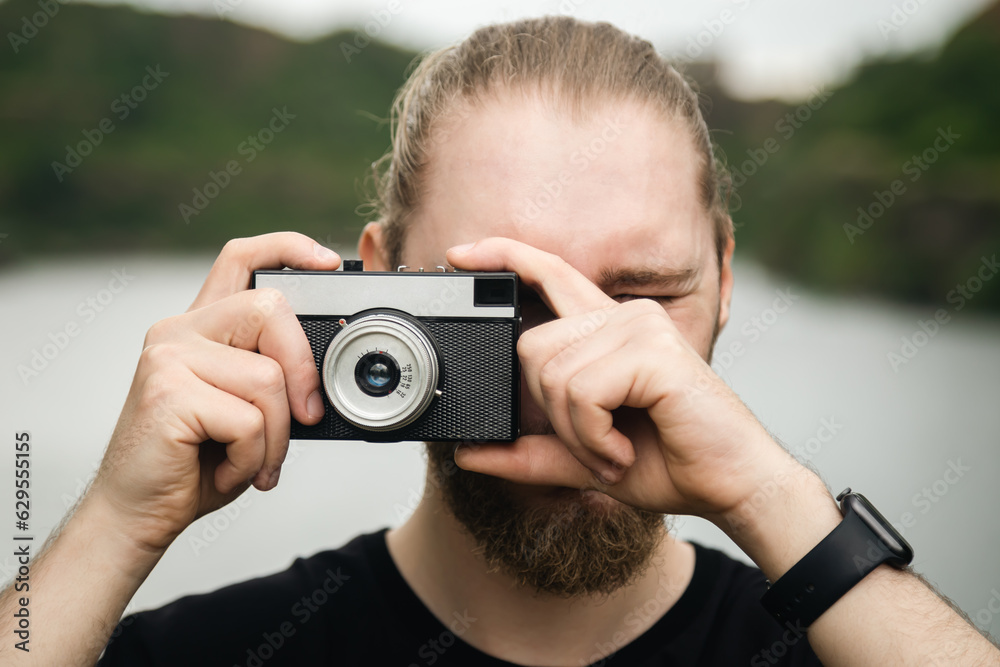 A young male photographer takes a photo on an old film camera on a blurred background of a river in a mountainous area, the concept of tourism. A young male photographer takes a photo on an old film camera on a blurred background of a river in a mountainous area, the concept of tourism.