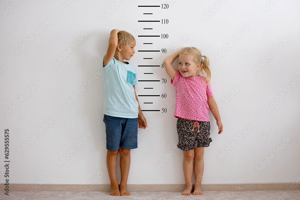 Φωτογραφία Little children, blond boy and girl, measuring height against wall in room