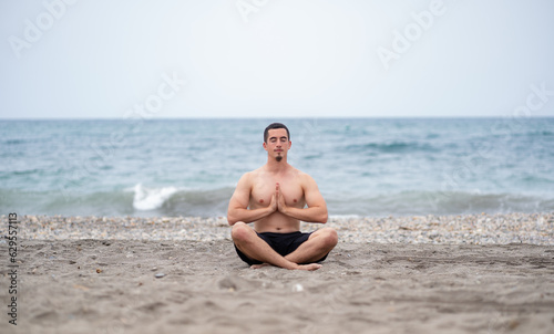 Young man shirtless doing the lotus pose with eyes closed on the beach
