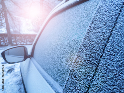 Window of the car covered with frost during winter and sun flare