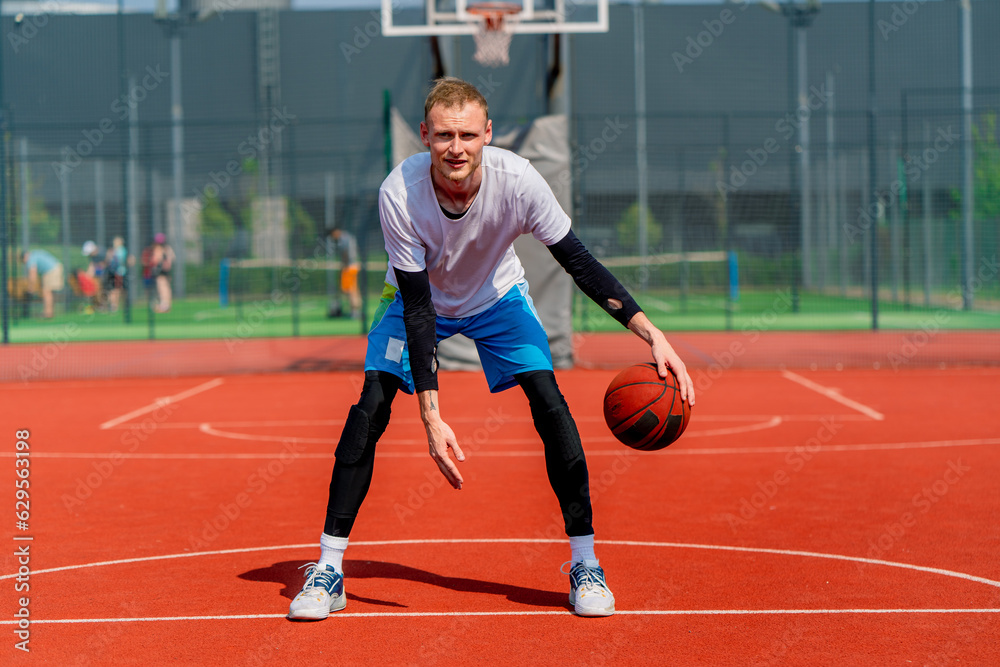 Obraz premium a Tall guy basketball player with the ball shows his dribbling skills during practice on the basketball court in the park 