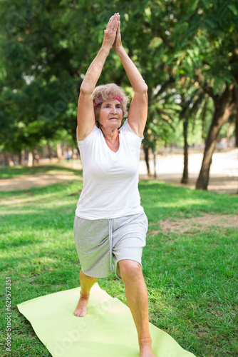 Old lady standing in warrior I yoga pose outdoors