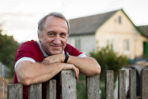 Mature man standing relaxed near fence in backyard smiling