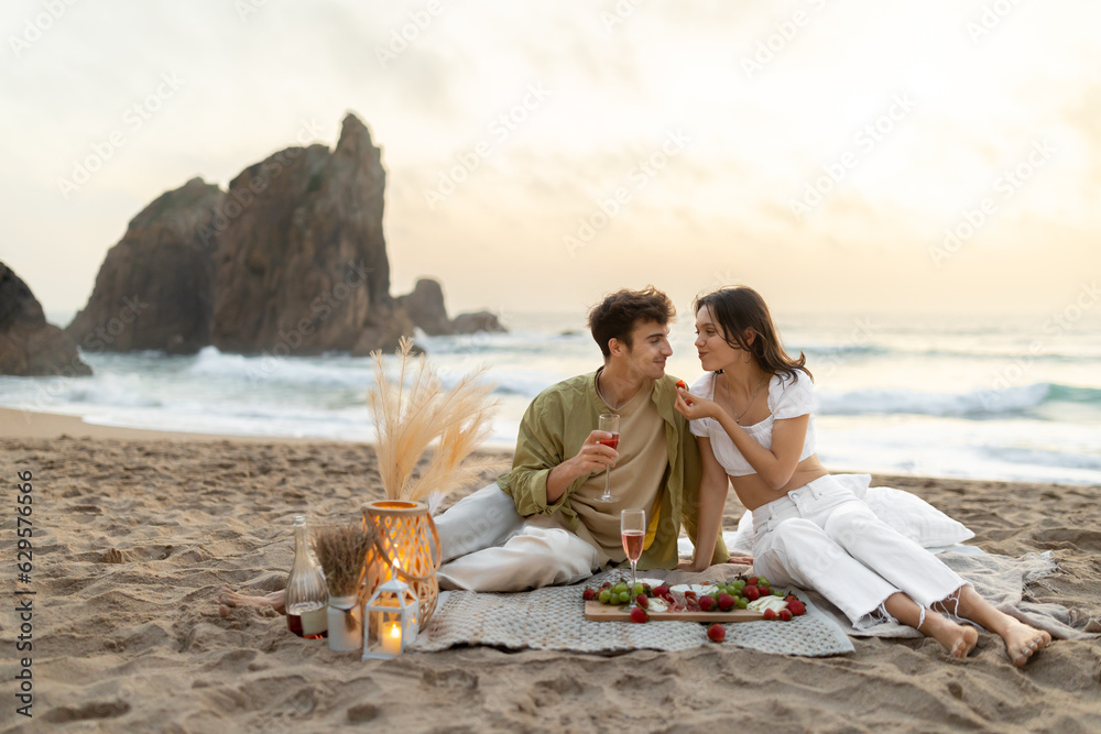Romantic young couple having picnic on sandy beach with ocean view ...