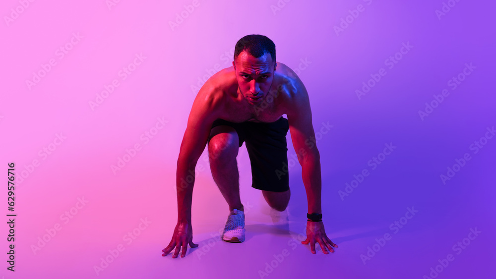 Black athlete man standing in crouch start position, neon light
