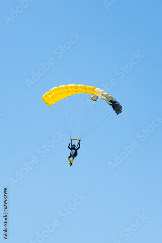 Obraz na płótnie Stunning view of of a skydiver with a yellow parachute and a blue sky in the background. w salonie