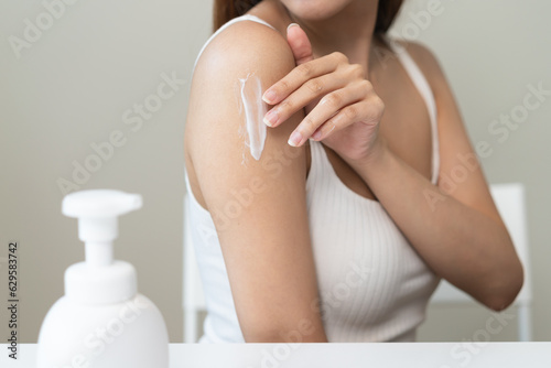 Body skin care routine concept. Close-up view hands of a young woman applying lotion cream on the shoulder photo