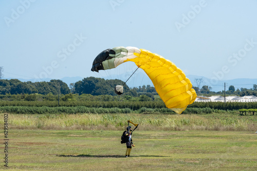 Stunning view of a skydiver with a yellow parachute landing on a green lawn during a sunny day.
