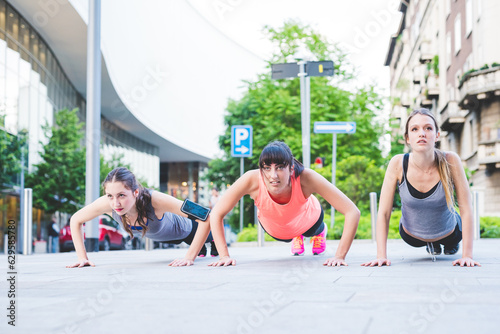 Three young beautiful caucasian millennials women outdoor in the city doing push ups - active, sport, fitness concept
