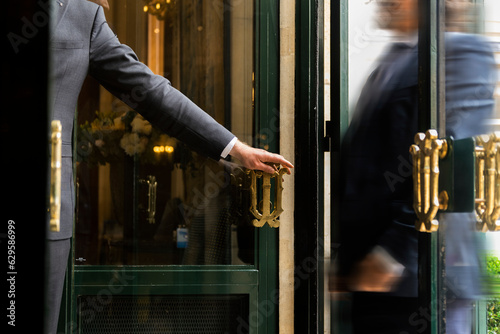 Luxury service gesture – Business man holding a door handle with blurred motion of a guest entering a high-end establishment