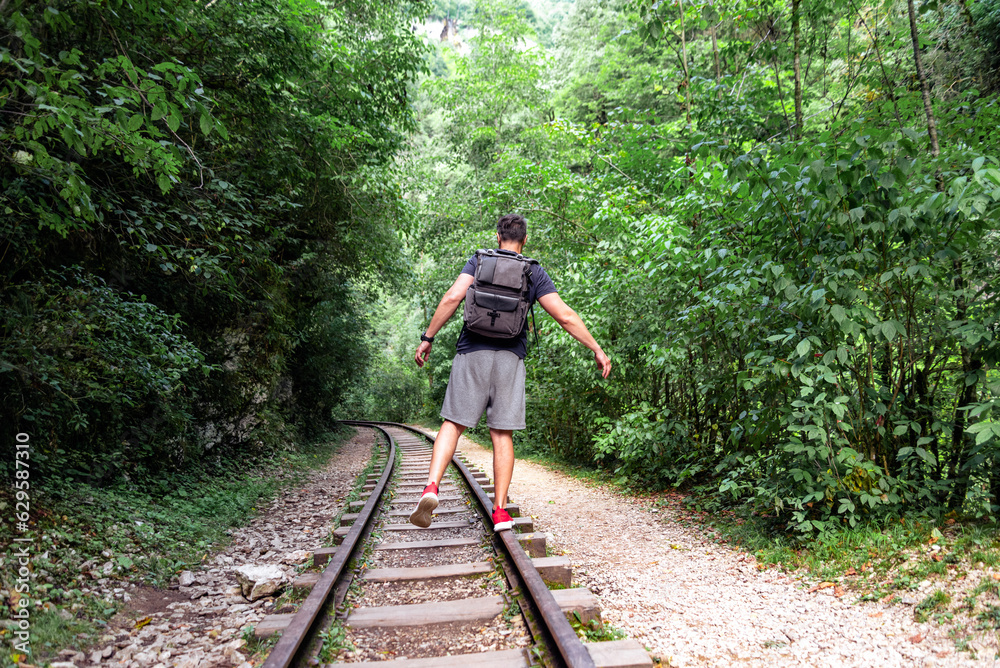 young male tourist walks on the railway in the jungle of thailand