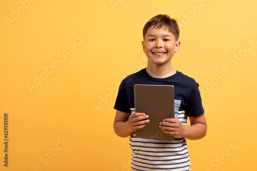 Positive cute school aged kid holding digital tablet, copy space photo