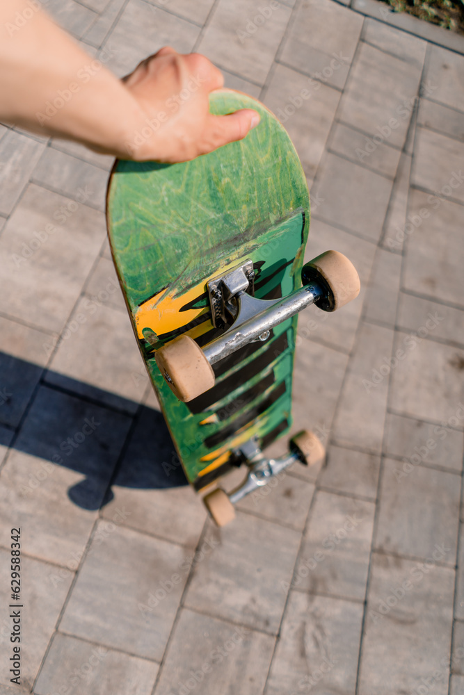 Close-up of a skateboard that a skateboarder holds in his hand in a public park the concept of adrenaline craving and the love of skateboarding 