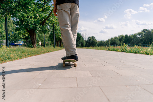 young guy skater rides a skateboard on the path of the city park against the background of trees and sky close-up © Guys Who Shoot