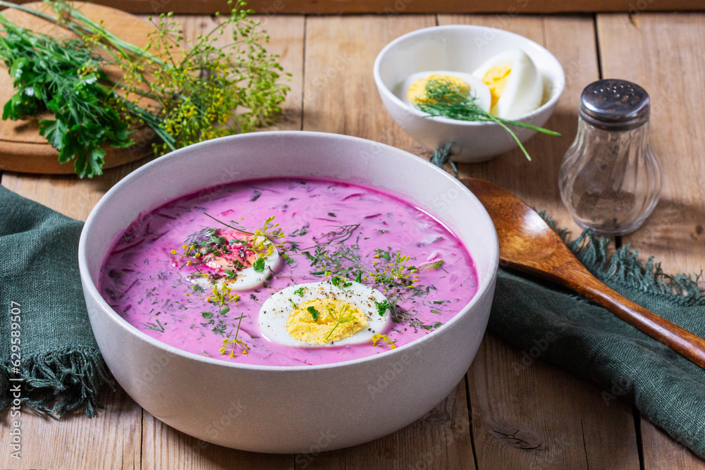 Traditional summer cold beetroot soup with cucumber, egg and sour cream on a wooden background. Rustic style.