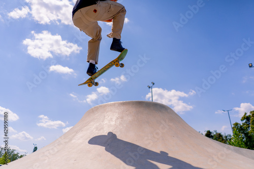 A young guy skater does a stunt on the edge of a skatepool against a backdrop of sky and clouds at a city skate park 