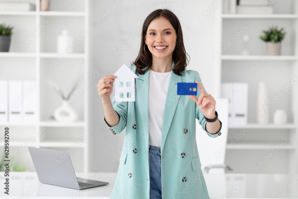 Cheerful young caucasian businesswoman in suit hold credit card and house Cheerful young caucasian businesswoman in suit hold credit card and house