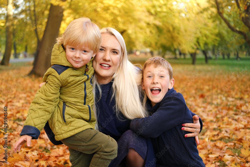 Fototapeta premium Happy mother is hugged by two sons. Family spending free time together in autumn park