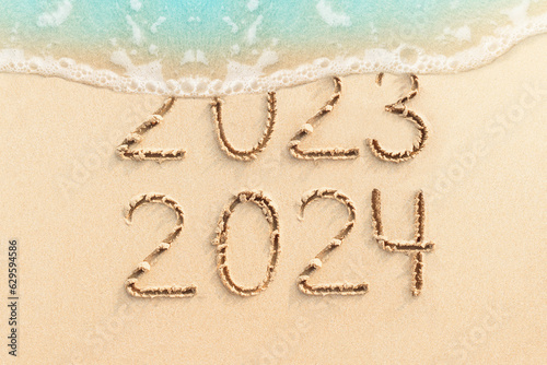 New Year 2024 concept photo. Numbers 2023 written on sandy beach with blue ocean wave on background. 