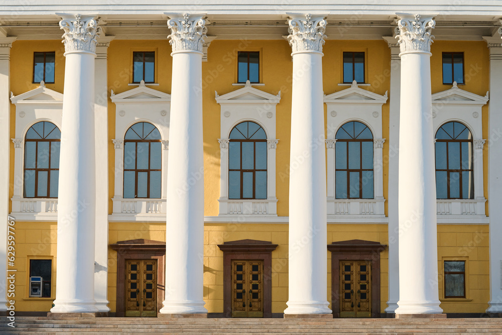 Obraz premium Front part of munucipal or cultural institution with white plaster columns, row of long arch shaped windows, wooden doors and yellow walls