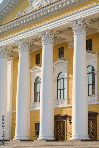 Part of cultural multi-storey institution with yellow walls, white plaster columns and row of closed wooden doors