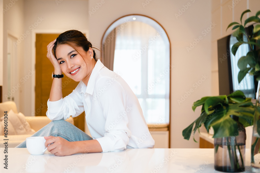 smiling woman holding coffee cup looking at camera. young woman drinking tea or cofffee in her kitchen while getting ready to go to work. smiling woman holding coffee cup looking at camera. young woman drinking tea or cofffee in her kitchen while getting ready to go to work.