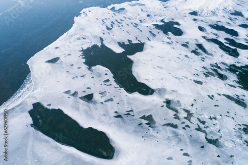 Abstract aerial view of amazingly shaped snow remains with gaps, on the ice of a frozen lake in winter, Reykjanes, Iceland. photo