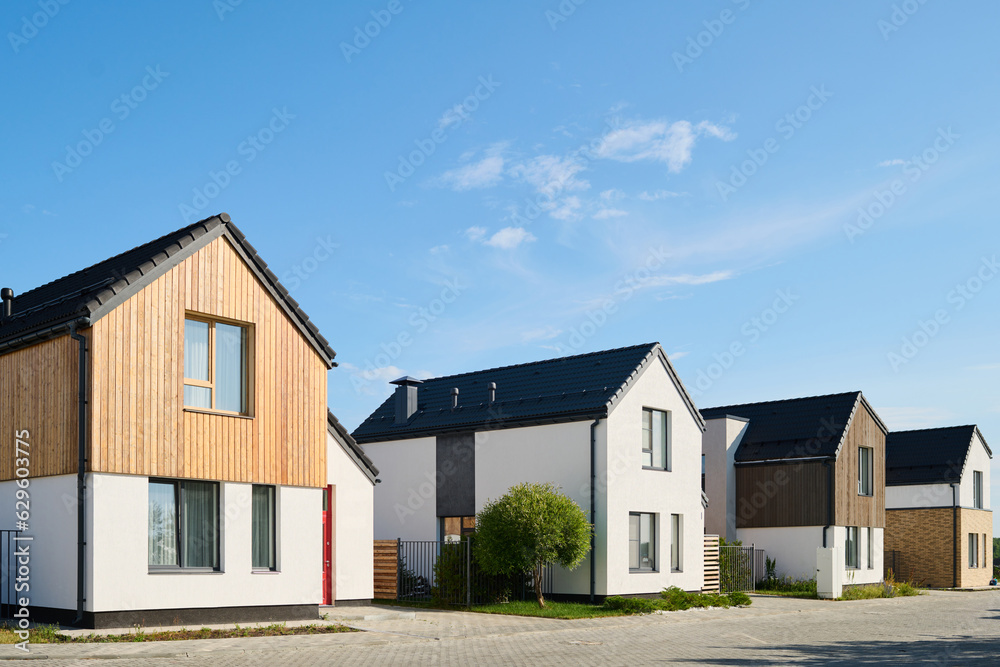Perspective view of several small houses standing in row in rural environment against blue sky on sunny day Perspective view of several small houses standing in row in rural environment against blue sky on sunny day