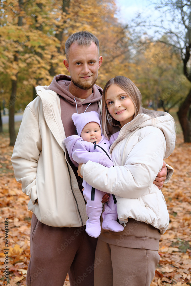 Young parents, mother and father, walk with a newborn baby in the autumn park. Parents smiling and looking at the camera