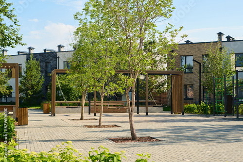 Fototapeta Naklejka Na Ścianę i Meble -  Row of green trees growing along pathway in deserted yard with playground surrounded by small two storey houses