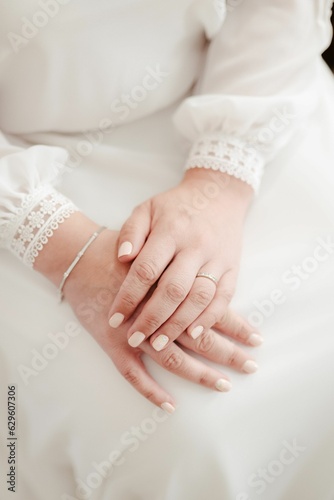 Young woman in wedding dress, sitting with her hands folded on her knees wearing an engagement ring