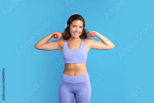 Happy slim young caucasian lady in sportswear enjoy body care  doing exercises for hands with dumbbells