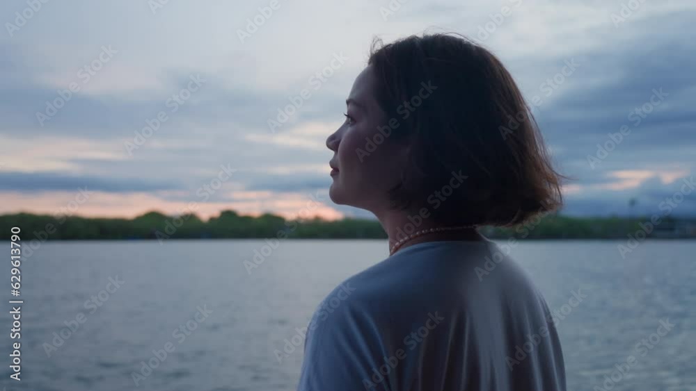Beautiful happy girl enthusiastically looking at evening sky on lake shore. A woman with short bob enjoys sunrise and smiles. Lonely female person feeling ecstasy. The delight of what he saw.