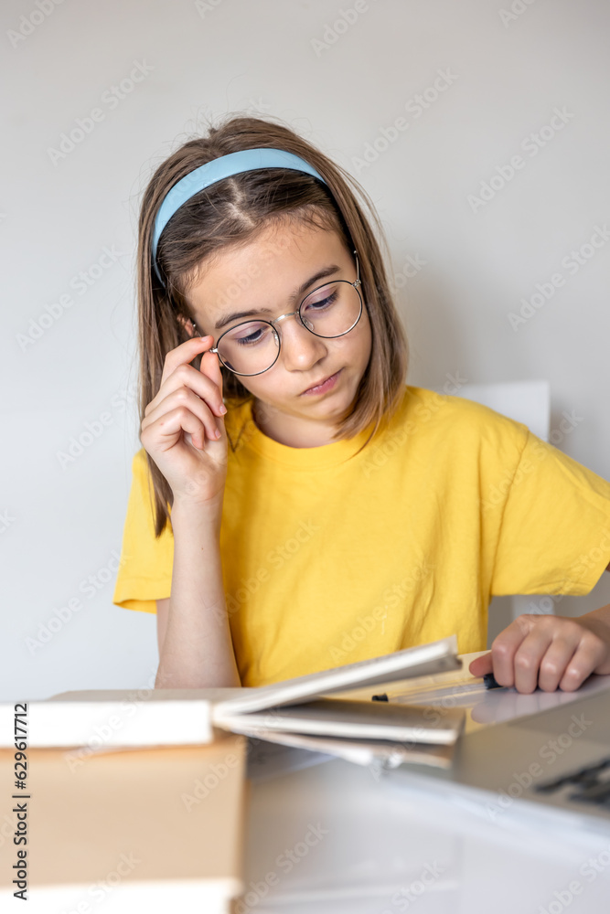 A teenage girl is doing homework with books and a laptop sitting at a table.