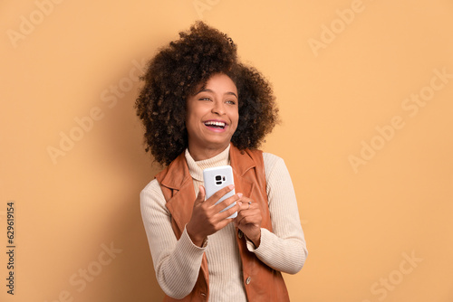 happy african american woman texting and typing on the mobile smartphone in beige colors. network, messaging, internet concept. photo