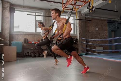 Strong man in training gloves with slender female doing stretching exercises in the gym and looking ahead